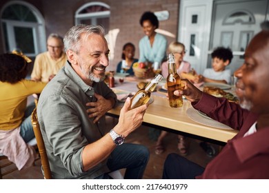 Happy man and his African American father in law toasting with beer during family meal at dining table. 