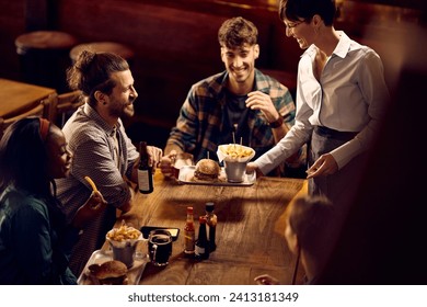 Happy man and his friends enjoying in drinks while waitress sis serving them burgers and French fries in bar. - Powered by Shutterstock