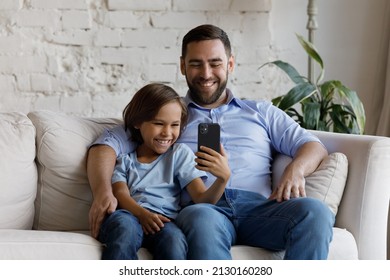 Happy man his little son sit on couch at home holding smartphone smiling looking at screen making video call, use new mobile application, take selfie picture, have fun use modern wireless tech concept - Powered by Shutterstock