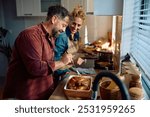 Happy man and his wife preparing roast turkey for Thanksgiving meal while cooking together in the kitchen.