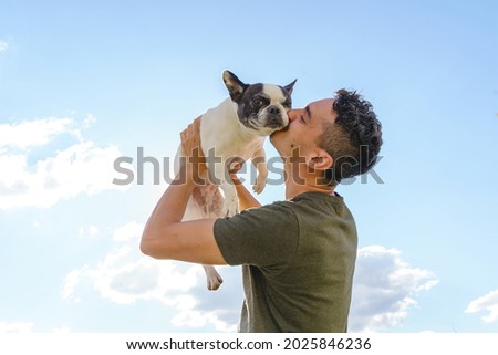 Happy man holding up a bulldog. Horizontal view of man with pet outdoors. Lifestyle with animals