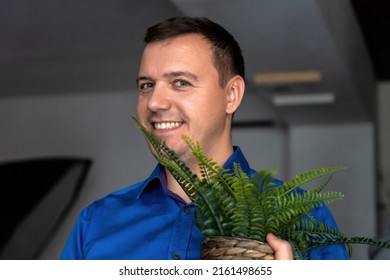 Happy Man Holding Fern House Plant. Successful Millennial Man, Dressed In Blue Shirt Holding Flower Pot With Green Fern Plant House And Looks At Camera