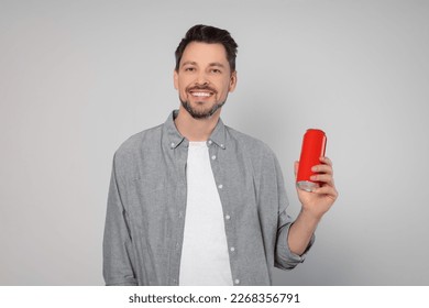 Happy man holding red tin can with beverage on light grey background - Powered by Shutterstock