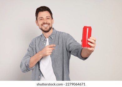 Happy man holding red tin can with beverage on light grey background - Powered by Shutterstock