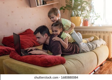 Happy Man With Joyful Children Using Laptop And Earphone During His Home Working While Sitting On Sofa At Home, Home Office With Together With Children, Life During Quarantine