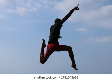 Happy man jumping. Blue sky background. Young cheerful Indonesian boy jumps. A teenager in a good mood jumps in the air. Sunny tropical day - Powered by Shutterstock