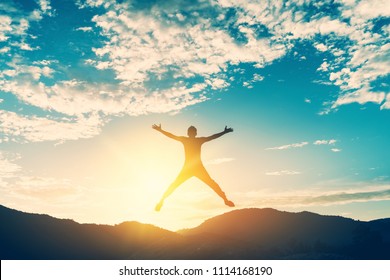 Happy man jumping at top of mountain with sunset sky abstract background. Freedom feel good and summer vacation concept. Vintage tone filter effect color style.