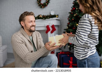 Happy Man In Knitted Cardigan Giving Gift Box To Blurred Daughter During Christmas At Home