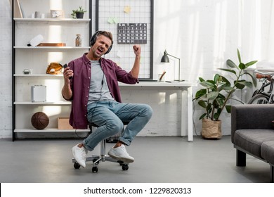 Happy Man Listening Music And Singing While Sitting On Chair At Home Office