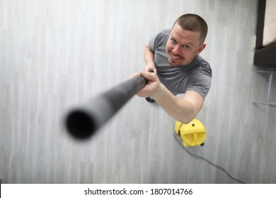 Happy Man Look Up And Smile At Home. Person Hold Black Hose From Yellow Vacuum Cleaner In His Hand And Lift It Up.