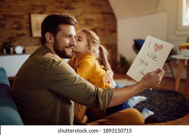 Happy man looking at daughter's drawing while she is kissing him Father's day at home  