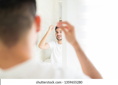 Happy Man Looking At His Reflection In Mirror While Setting Hair