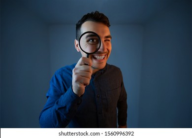 Happy man with magnifying glass on grey background. Curious young man with magnifying glass Isolated on grey background. - Shutterstock ID 1560996392
