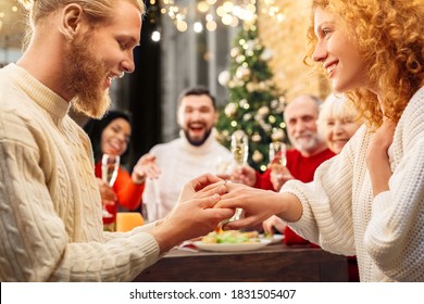 Happy man making propose and puts wedding ring on woman finger. Smiling couple celebrating engagement in family circle and friends - Powered by Shutterstock