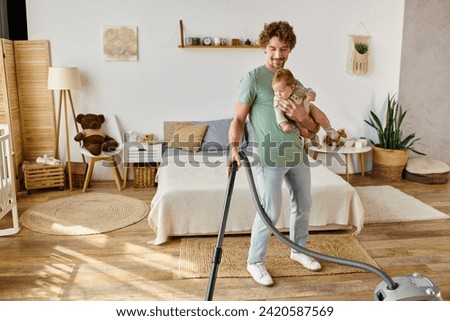 happy man multitasking housework and childcare, father vacuuming bedroom with infant son in arms