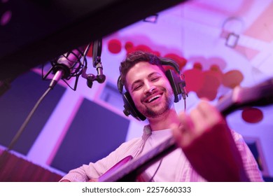 Happy man, musician or guitar in neon studio, recording production or performance for radio, label or low angle concert. Guitarist, artist or singer playing strings instrument on headphones practice - Powered by Shutterstock