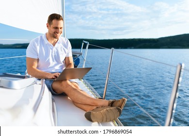 Happy Man On Yacht Sitting With Laptop Working Living On Sailboat During Summer. Liveaboard Tour. Empty Space For Text