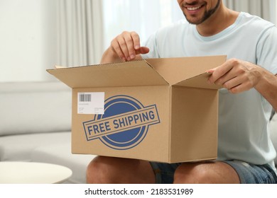 Happy Man Opening Parcel On Sofa At Home, Closeup. Free Shipping