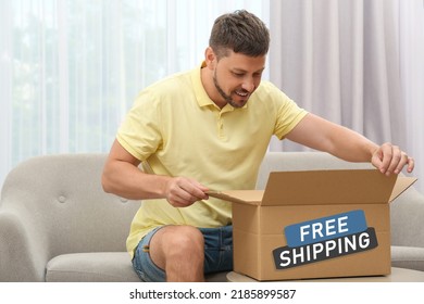 Happy Man Opening Parcel On Sofa At Home. Free Shipping