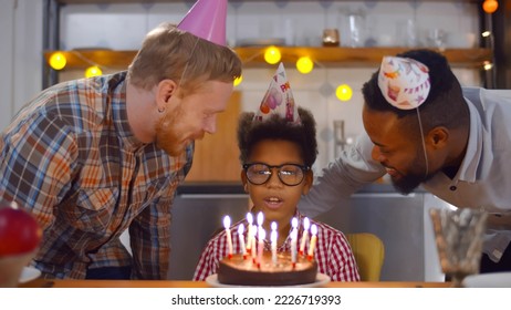 Happy man parents celebrating son birthday together at home. Happy african preteen boy making wish and blowing out candles on birthday cake celebrating wit multiethnic gay parents - Shutterstock ID 2226719393