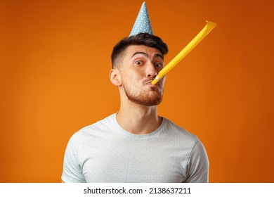 Happy man with party cone blowing into party horn - Shutterstock ID 2138637211