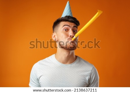 Happy man with party cone blowing into party horn