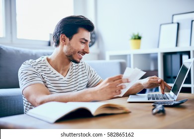 Happy man paying bills on his laptop in living room