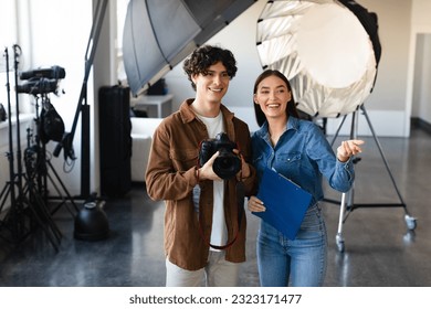 Happy man photographer and female art director discussing models and talking about the photoshoot, looking aside and smiling, standing near modern lighting equipment, copy space - Powered by Shutterstock