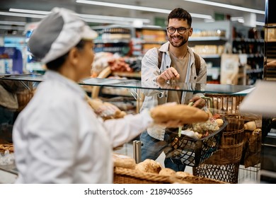 Happy man pointing at bread he wants to buy while talking to a baker in supermarket bakery.  - Powered by Shutterstock