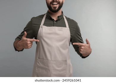 Happy man pointing at kitchen apron on grey background, closeup. Mockup for design