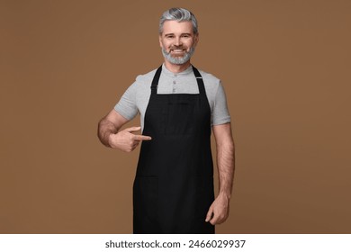 Happy man pointing at kitchen apron on brown background. Mockup for design