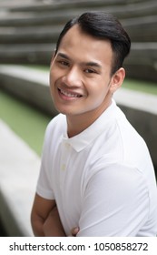 Happy Man Portrait, Smiling Friendly Man, Happy Handsome Man Sitting Smiling In City Environment; Young Adult South East Asian Man Model With Tan Skin And Short Hair