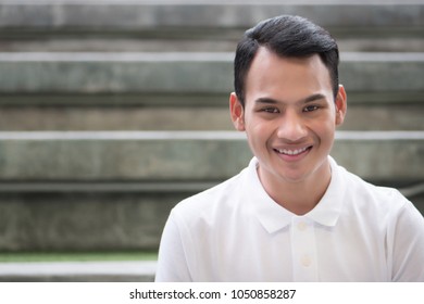 Happy Man Portrait, Smiling Friendly Man, Happy Handsome Man Sitting Smiling In City Environment; Young Adult South East Asian Man Model With Tan Skin And Short Hair