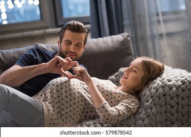 Happy man and pregnant woman showing heart sign with fingers