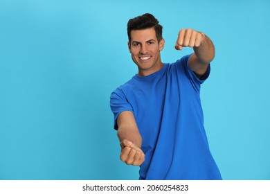 Happy man pretending to drive car on light blue background. Space for text