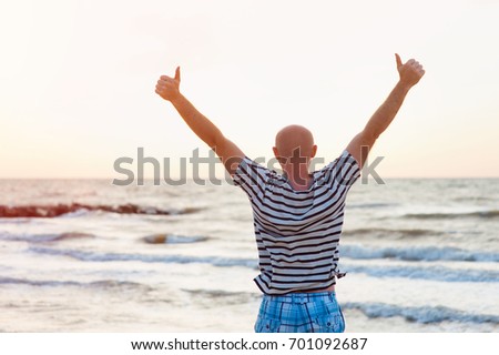 Happy man raises his arms up against the sea