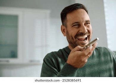 Happy man recording voice message on mobile phone in the kitchen. Copy space.  - Powered by Shutterstock