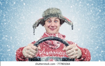 Happy man in red sweater and hat with a steering wheel, snow blizzard. Concept car driver 