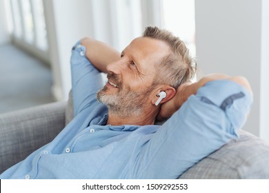 Happy Man Relaxing Listening To Music On Ear Buds Lying Back On A Comfy Sofa With A Smile Of Pleasure