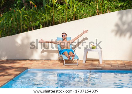 Happy man relaxing on sunbed close to swimming pool. 