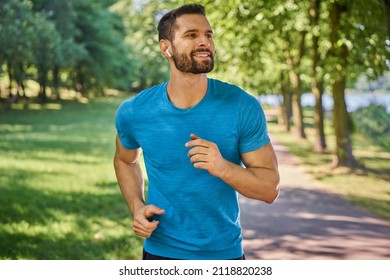Hombre feliz corriendo en el parque escuchando música en auriculares en un día soleado de verano
