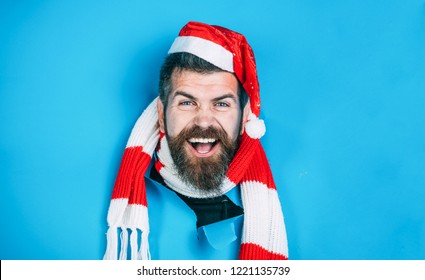 Happy man in Santa hat looking through hole in paper. Christmas, New Year, holidays, winter concept. Stylish guy in santa hat&scarf. Smiling guy in Santa hat breaks through paper wall. Christmas sales