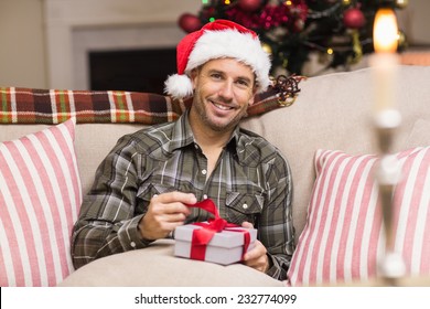 Happy Man In Santa Hat Opening A Gift At Home In The Living Room