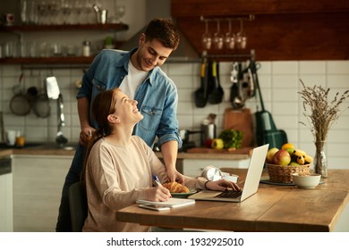 Happy Man Serving Croissant To His Wife Who Is Working On A Computer At Home.