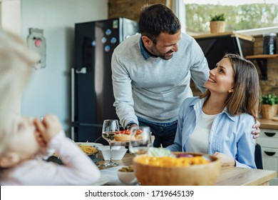 Happy Man Serving Food And Talking To His Wife While Having Family Lunch At Dining Table. 