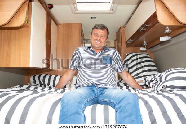 Happy man sitting in bed of camping car\
motorhome in vanlife style in modern\
campervan