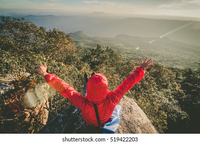 Happy man sitting on a cliff side with arms raised up