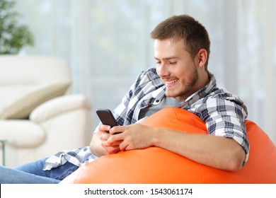 Happy Man Sitting On An Orange Pouf At Home Using Mobile Phone