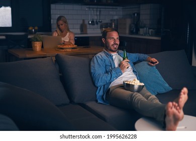 Happy Man Sitting On Sofa With His Feet On Table, Holding Beer And Relaxing While Watching TV