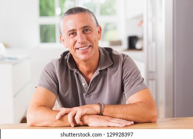 Happy Man Sitting At Table In Kitchen